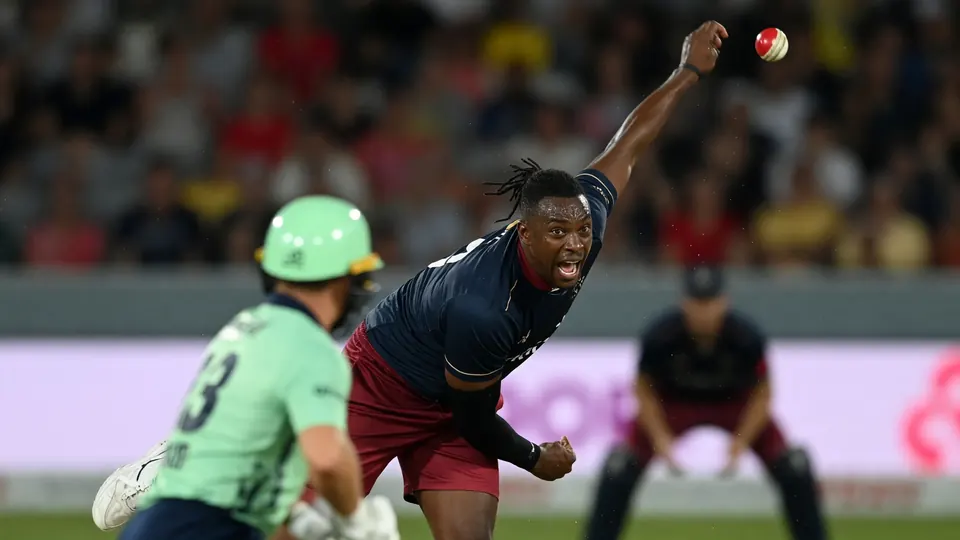 Cricket batter swinging through a delivery under stadium lights with a blurred crowd behind
