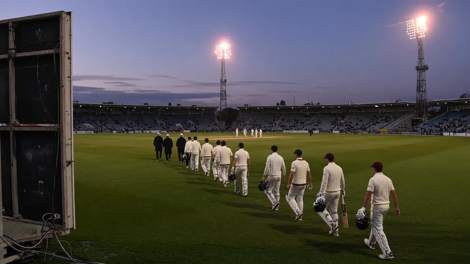 Cricketers walking onto the field at dusk as stadium lights warm up
